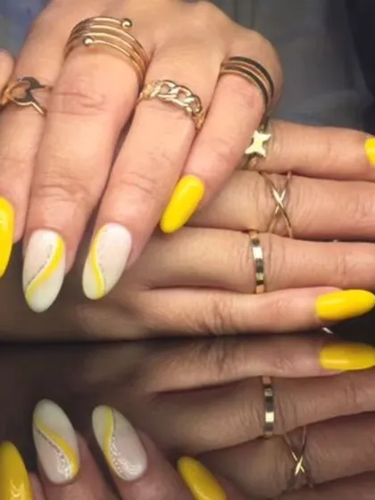 A bright and sunny manicure with yellow nails and white accent nails featuring yellow swirl designs.