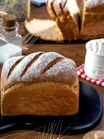 A classic loaf of white bread with a flour-dusted, scored top. The image is styled with milk and flour to emphasize the fresh, from-the-bakery feel, focusing on the simple beauty of a well-baked loaf.