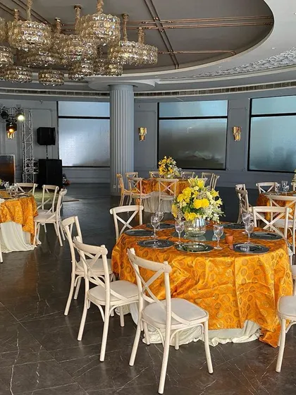 A bright and cheerful Haldi or Mehendi lunch setup in a modern ballroom. The vibrant yellow tablecloths and floral centerpieces pop against the neutral chairs, while unique chandeliers add a touch of contemporary flair.