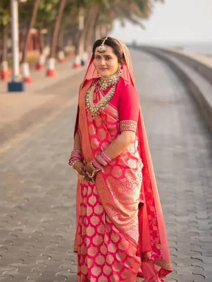 A full-length shot of the bride by the sea. The traditional red saree and her elegant makeup create a timeless and iconic bridal portrait.