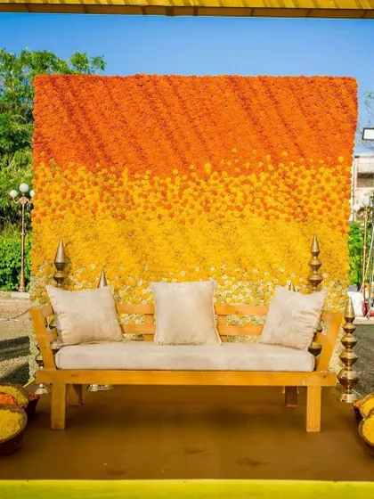 A minimalist yet impactful photo backdrop for a Haldi. The wall is made of ombre-toned marigolds, creating a beautiful and modern look.