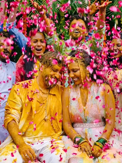 The couple is showered with a cascade of pink petals by their friends and family, creating a picture-perfect, vibrant Haldi moment.
