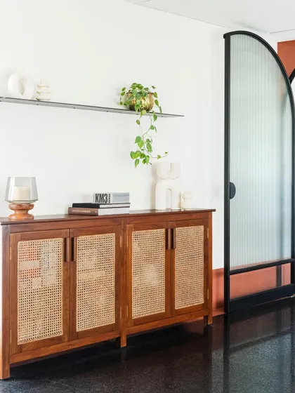 The dining area also features this beautiful cane-fronted credenza for storage. The arched glass door in the background adds another layer of architectural detail and reflects the light.
