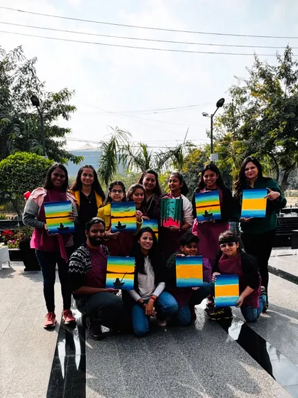A group shot from a sunny outdoor workshop. Everyone is proudly holding up their sunset paintings.