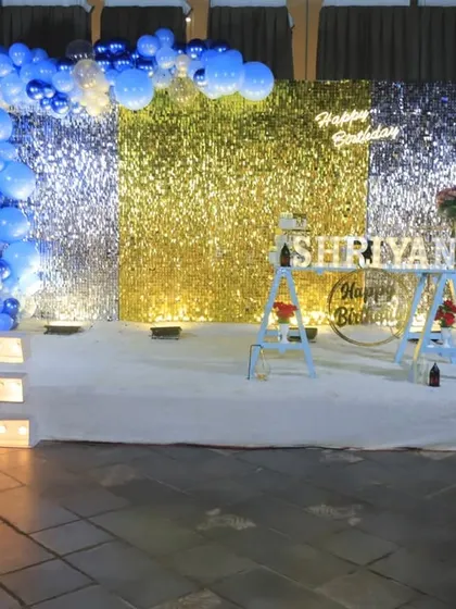 A glamorous first birthday setup using a gold and silver sequin wall as the centerpiece. The stage is completed with large marquee letters and a touch of royal blue in the balloon decor.