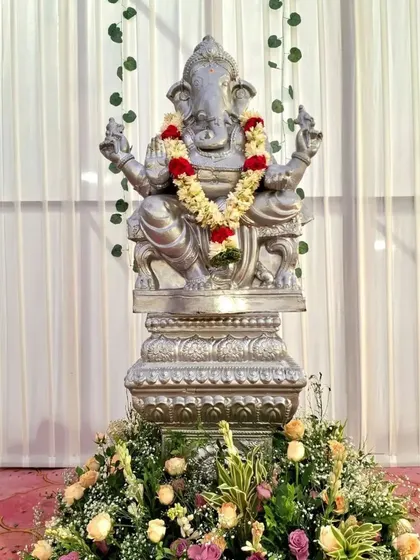 A simple and elegant setup for a Ganesha idol during a wedding. The statue is placed on a pedestal with floral decorations, against a clean white backdrop.