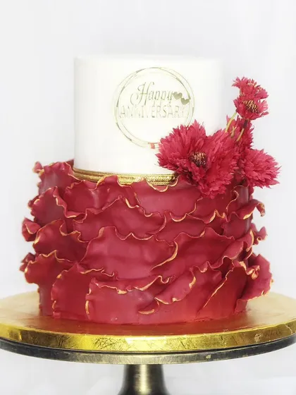 A bold and dramatic anniversary cake with a striking contrast of white and deep red. The bottom tier features intricate, hand-ruffled fondant, creating a design that is both modern and romantic.