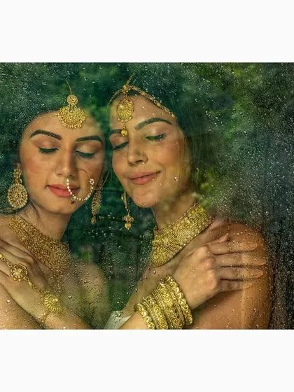 An atmospheric mood shot for a jewellery campaign. The models, adorned in gold, are photographed through a rain-streaked surface to create a soft, intimate, and romantic feeling.