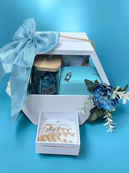 A beautiful gift hamper in shades of blue. This set, presented in a white hexagonal box, includes jewelry and other curated items, all tied together with a large, elegant blue bow.