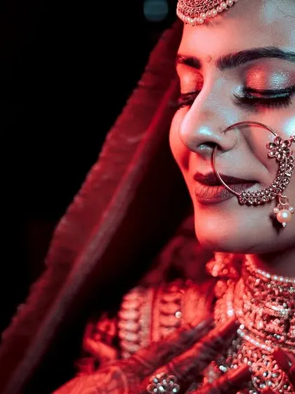 A stunning close-up of the bride under dramatic red lighting. This shot highlights her flawless makeup, intricate jewelry, and the serene expression of a bride ready for her new beginning.