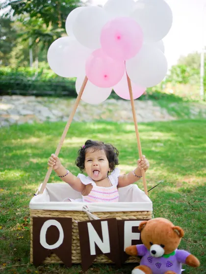 A playful moment from an outdoor first birthday shoot. The hot air balloon prop adds a touch of whimsy and fun to this sunny celebration.