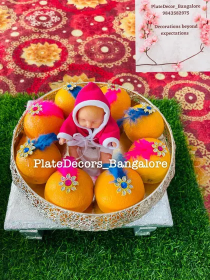 Oranges decorated with colorful feathers and floral motifs for a baby shower. The sleeping baby doll in the middle makes this platter extra special.