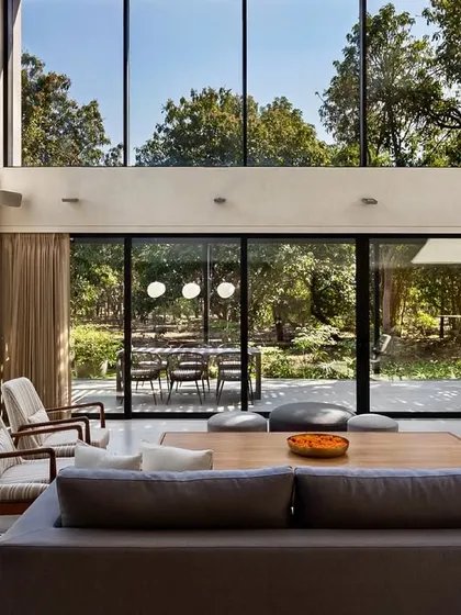 The floor-to-ceiling glass walls of the Mango Orchard House living room perfectly frame the lush, green landscape, making it a dominant feature of the interior.