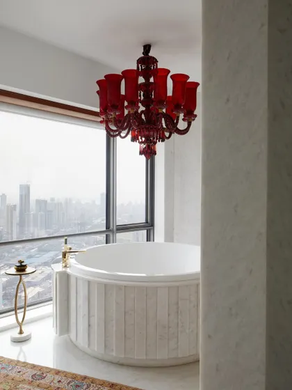 In this master bathroom high above the Mumbai skyline, luxury meets drama. A vintage red Murano glass chandelier hangs over a custom marble spa bath, creating a romantic and intensely personal retreat with an unparalleled view of the city.