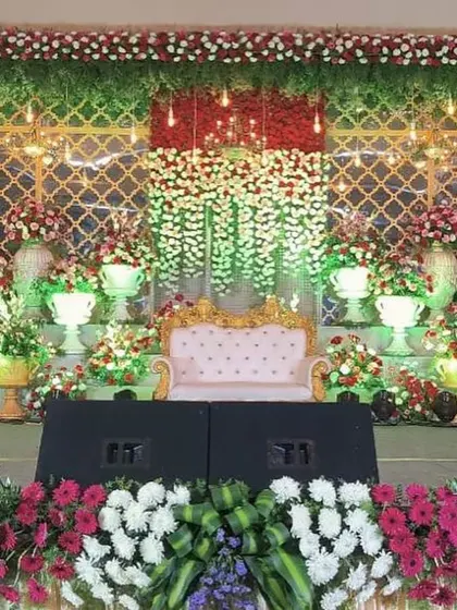 A vibrant and colorful stage decoration featuring a mix of red, white, and green flowers against a gold jaali backdrop. This design is perfect for an engagement or Sangeet ceremony.
