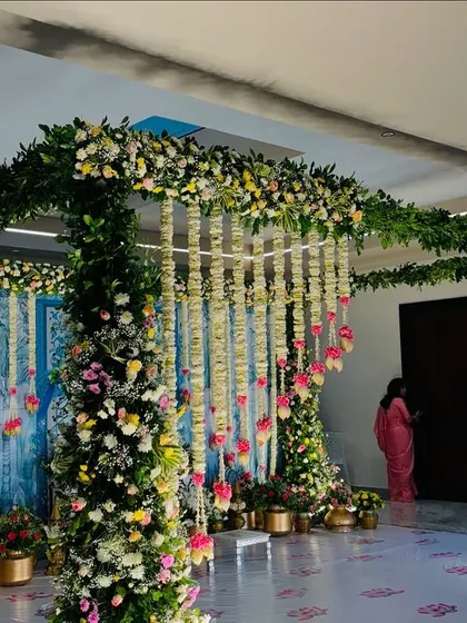 A wide view of an indoor stage with a Pichwai-style backdrop and lush floral pillars.