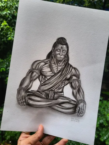 Holding the finished Hanuman sketch against a natural green background, which makes the powerful black and white figure stand out.