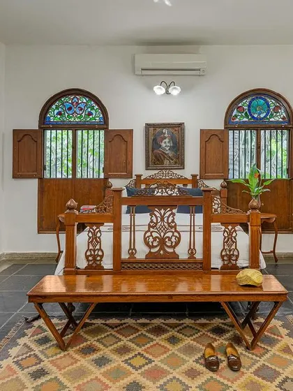 A wider view of the Vasishta suite, showcasing the spacious layout, antique vanity, and beautiful stained-glass windows that let in dappled light.