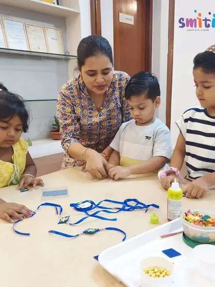 A teacher assists a group of children as they choose materials for their Rakhis. We provide a variety of colorful beads, threads, and shapes to spark their creativity.