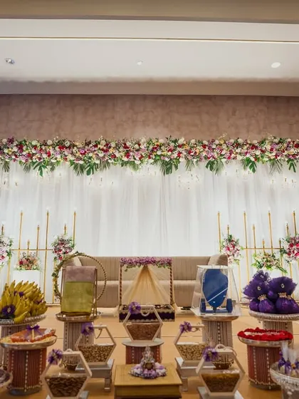 An elegant indoor setup for a traditional ceremony, with a beautiful floral stage backdrop and a vast array of offerings meticulously arranged in the foreground.