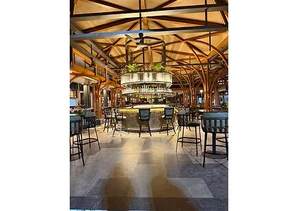 A wide shot of the bar and lounge area at KGA. The design uses natural materials like wood and stone, complemented by lush greenery, to create a space that feels both luxurious and grounded in nature.