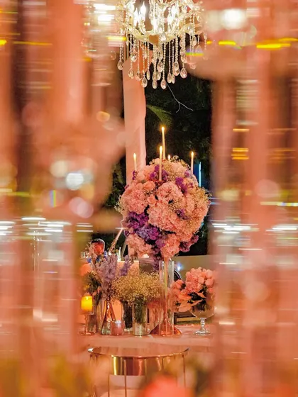 An artistic shot of the floral centerpiece seen through a screen of glass candelabras. This perspective highlights the layers of the design and the beautiful distortion of light and color.