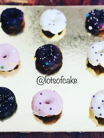 An assortment of mini donut cakes decorated with different coloured glazes and sprinkles. They are a fun and colourful treat for birthday parties.