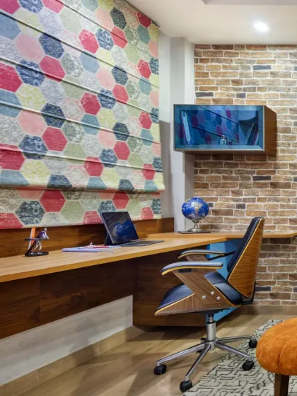The cantilevered workstation in the den, set against an exposed brick wall and a colorful hexagonal-patterned roman blind. This corner is designed for focus and productivity, without sacrificing style.