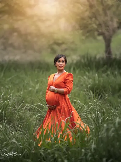 A duplicate of ID 33, this solo outdoor portrait captures an expecting mother in a vibrant orange dress amidst tall green grass, with soft, golden light giving it a dreamy quality.