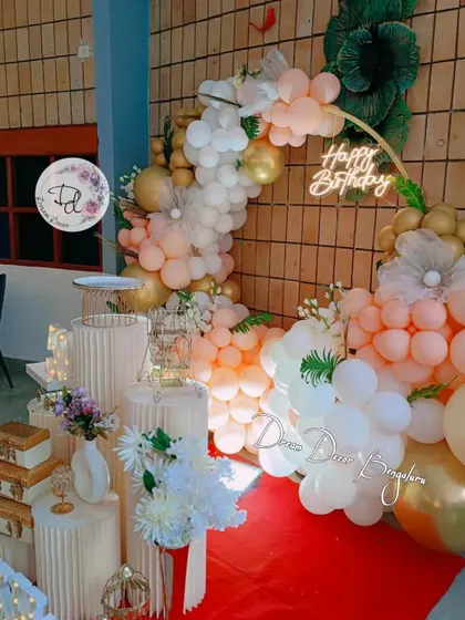 A classy birthday setup with a half-arch of peach and white balloons against a brick wall.