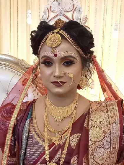 A classic Bengali bridal portrait. The look is defined by the traditional 'chandan' art on the forehead, kohl-rimmed eyes, and layers of beautiful gold jewelry.