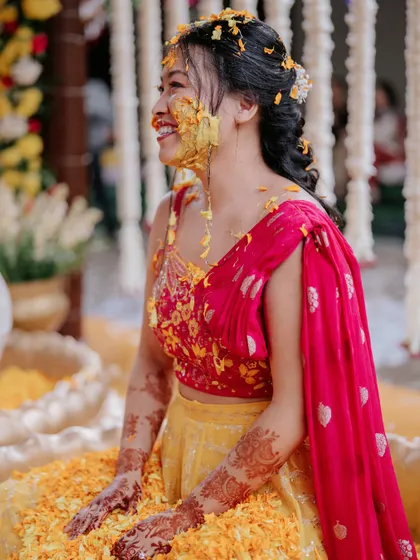The bride, covered in turmeric and flowers, sits in a lotus-shaped urli, fully embracing the fun and tradition of the Haldi ceremony.