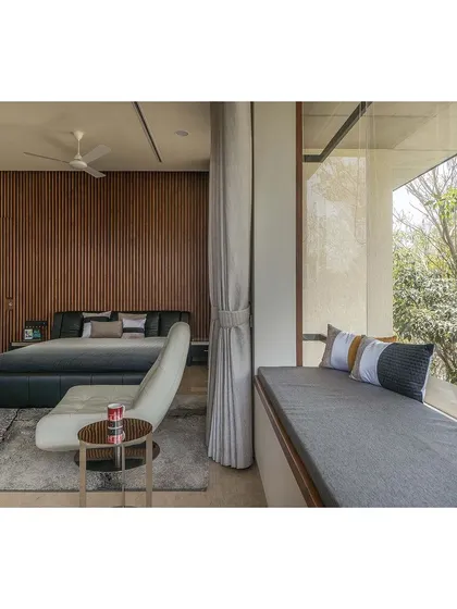 This bedroom in a Bengaluru home uses a monochromatic palette with shades of grey, complemented by a warm, fluted wood wall. A cozy window seat provides a perfect nook for reading while enjoying the view.