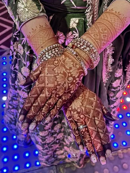 A stunning photo of a bride's hands, showcasing the deep, mature stain of her mehndi against the backdrop of her wedding attire.