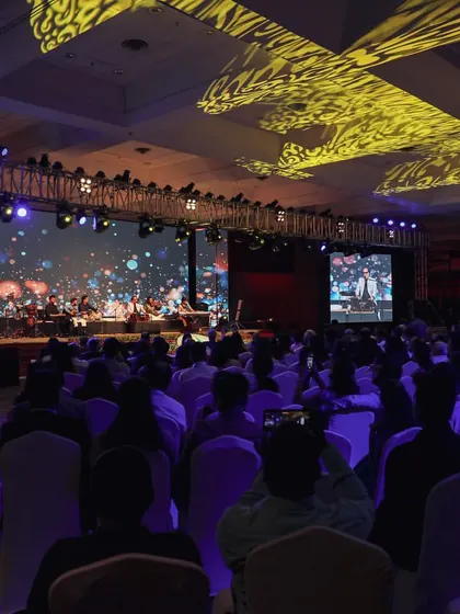 A wide shot of the audience enjoying the Talat Aziz ghazal evening. The large screens and professional lighting show the scale of this corporate event.
