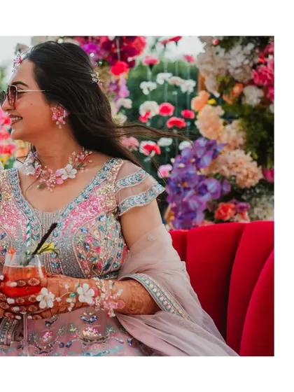 The bride enjoying a drink during her Mehendi ceremony. Her floral jewelry and colourful lehenga perfectly match the festive and relaxed vibe of the event.