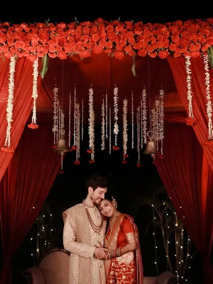 A perfect final shot for a wedding album. The couple stands under their magnificent red floral mandap, sharing a quiet, loving embrace after the ceremony is complete.