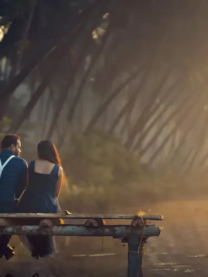 A serene pre-wedding moment as a couple sits on a wooden pier, watching the sunrise together.
