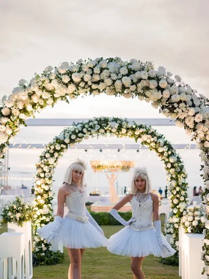 Welcome artists in angelic white outfits greet guests at the entrance of the all-white floral archway for a Goa sundowner.