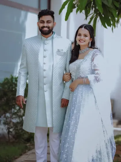 A full-length portrait of a smiling couple in matching light blue outfits.