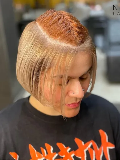 A playful peekaboo hair colour. This style features a bold orange braid hidden within a chic blonde bob, offering a fun surprise and a unique touch of personality.