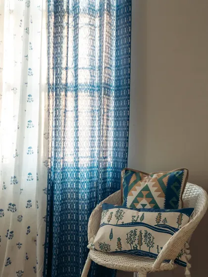 A close-up of our layered blue curtains and coordinating cushions. The mix of a bold ikat-style print with a subtle floral sheer adds depth and character to this bedroom corner.