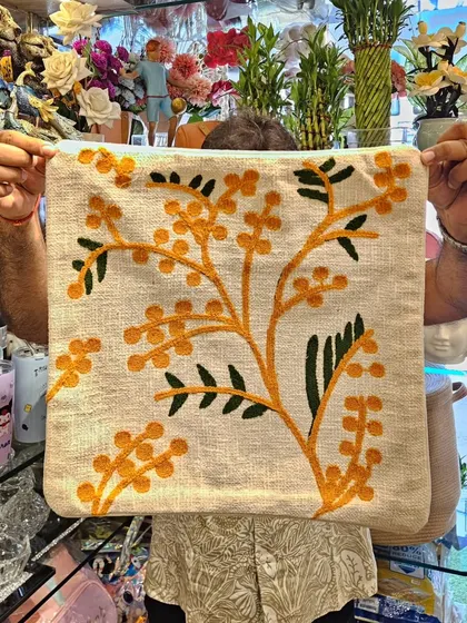 A beautiful hand-embroidered cushion cover with a yellow mimosa branch design. It's a subtle yet cheerful way to bring a bit of nature's beauty inside.
