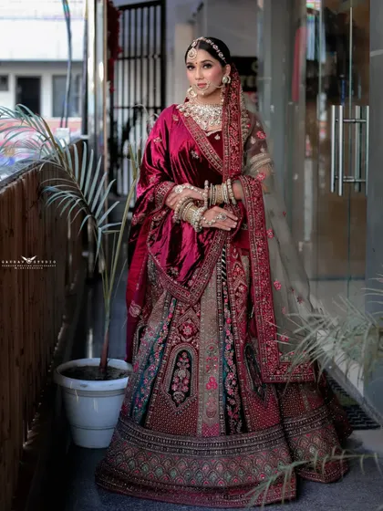 A confident, full-length pose of the bride in her multi-toned velvet lehenga. The outdoor setting provides natural light that enhances the intricate embroidery of her outfit.