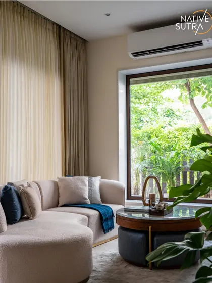 A detail shot of the contemporary TV lounge, focusing on the layered textures. The plush, curved sofa is complemented by soft cushions and a view of the greenery outside, creating a perfect blend of comfort and nature.