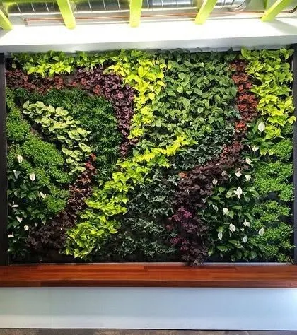 An indoor vertical garden installed as a living art piece. The design uses a variety of plant textures and colors to create a natural, flowing pattern, set above a wooden bench.