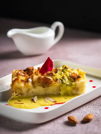 A slice of Shahi Tukda, a traditional Indian bread pudding, elegantly plated with a drizzle of rabri and garnished with a rose petal.
