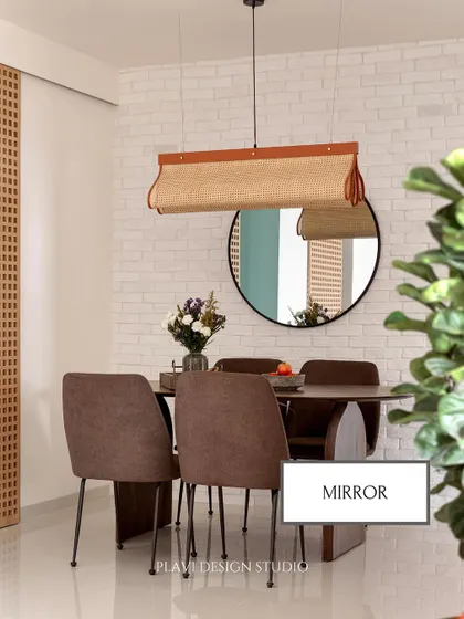 This dining area features a custom pendant light made of rattan and leather, hanging over a simple wooden table. The round mirror reflects the light and adds a soft, organic shape to the wall.