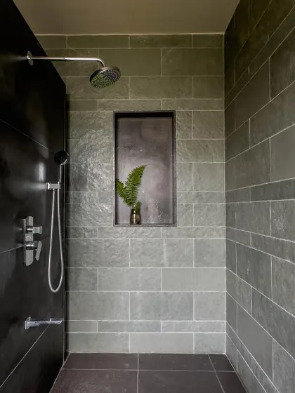 The walk-in shower is clad in grey Kota stone tiles, with a built-in niche for storage. The minimalist chrome fixtures and simple design create a clean, modern look.