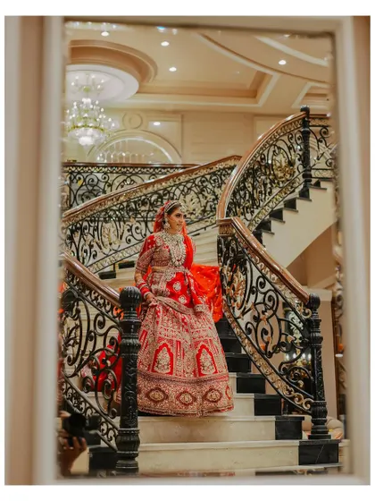 A beautiful portrait of the bride on the staircase, viewed through a doorway. This creative framing adds depth and a sense of looking in on a private, elegant moment.